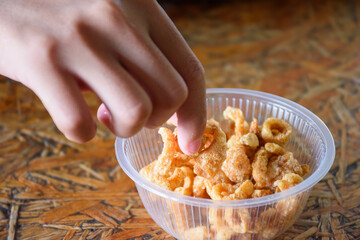 Close up of hand picking a Pork snack, Pork rind, Pork scratching or crackling in bowl on wooden background, Thai food, Thai stys, Eat with noodles.