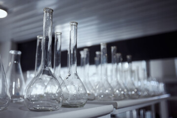 Row of various glass beakers and flasks, arranged on a laboratory bench in a dimly lit room. Foundation for a perfect brew. Concept of beer, brewery, manufacture, quality control
