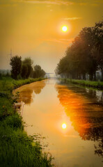 A tranquil sunset casts a warm glow on a winding river, surrounded by lush greenery and towering trees