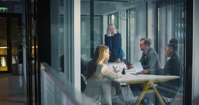 Footage from Outside the Glass Meeting Room: Managers and Specialists Having a Business Meeting in the Office. Female Project Manager Making an Analytical Sales and Marketing Presentation