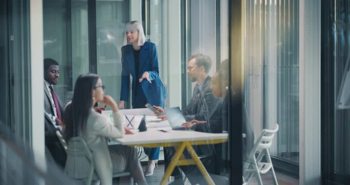 Group of Corporate Workers Analyzing Milestones of a Marketing Campaign. Young Beautiful Female Presenting Data and Results to Supervisors, Employees Having Conversations in a Glass Meeting Room