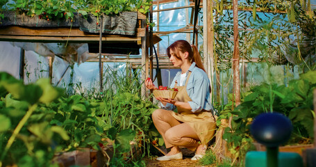 Portrait of female farmer wearing apron works in greenhouse full of plants. Beautiful Caucasian...