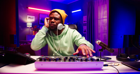 Close up portrait of handsome African male wearing yellow hat sits at table with DJ equipment in...