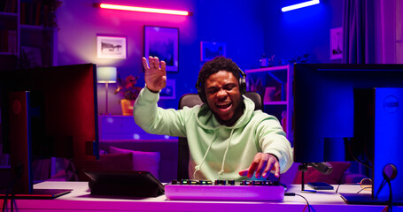 Close up portrait of satisfied African male wearing headphones creates modern music using DJ mixer....