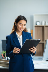 Fototapeta premium Business woman standing at her desk, reading stats and graphs on paperwork at the office.