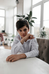 Obraz premium A thoughtful boy in a white shirt sitting at a table in a sunlit room filled with plants