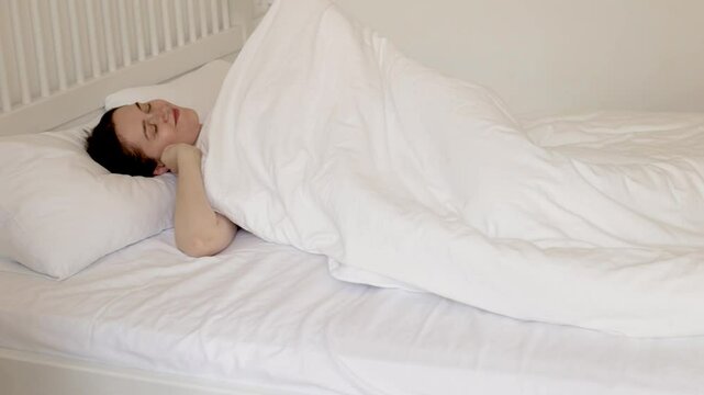 young caucasian woman lying in bed on white sheets and waking up early in the morning