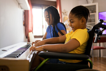 Two dark-skinned brothers are playing an electronic piano in their living room. The disabled child in a wheelchair is in the foreground.Concept of young africans playing a piano.