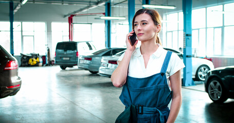 Close up portrait of young Caucasian female wearing working form speaks on phone with customer. Beautiful woman has conversation on gadget after repairing car.