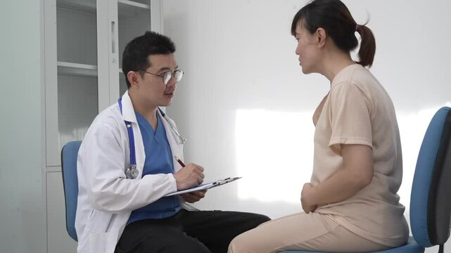 Asian female doctor listens to belly of pregnant mother during a prenatal exam in clinic. doctor provides caring advice, ensuring the health and happiness of the expecting mother and baby.