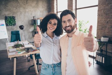 Photo of two young colleagues embrace demonstrate thumb up loft interior office business center indoors
