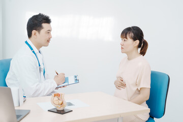 Asian female doctor listens to belly of pregnant mother during a prenatal exam in clinic. doctor...
