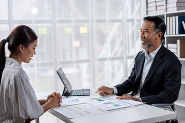 A man and a woman are sitting at a desk with a laptop