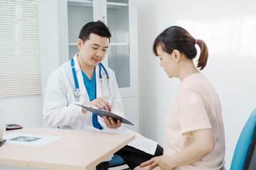 Asian female doctor listens to belly of pregnant mother during a prenatal exam in clinic. doctor provides caring advice, ensuring the health and happiness of the expecting mother and baby.