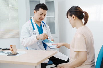 Obraz premium Asian female doctor listens to belly of pregnant mother during a prenatal exam in clinic. doctor provides caring advice, ensuring the health and happiness of the expecting mother and baby.