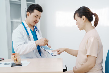 Asian female doctor listens to belly of pregnant mother during a prenatal exam in clinic. doctor provides caring advice, ensuring the health and happiness of the expecting mother and baby.