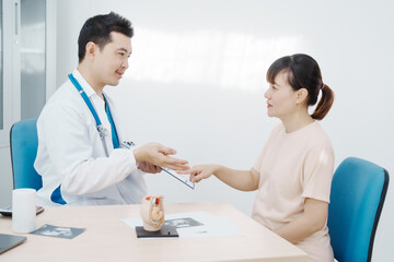 Asian female doctor listens to belly of pregnant mother during a prenatal exam in clinic. doctor...