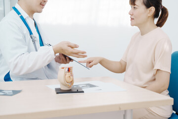 Asian female doctor listens to belly of pregnant mother during a prenatal exam in clinic. doctor provides caring advice, ensuring the health and happiness of the expecting mother and baby.