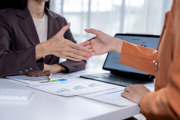 Businesswomen shaking hands over desk with laptop and documents