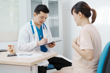 Asian female doctor listens to belly of pregnant mother during a prenatal exam in clinic. doctor provides caring advice, ensuring the health and happiness of the expecting mother and baby.