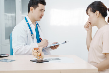 Asian female doctor listens to belly of pregnant mother during a prenatal exam in clinic. doctor provides caring advice, ensuring the health and happiness of the expecting mother and baby.