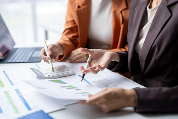 Two businesswomen analyzing financial charts and using calculator in office