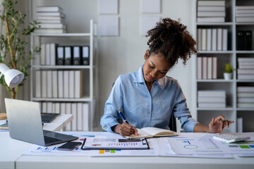 A woman is sitting at a desk with a laptop and a notebook