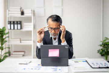 A man in a suit is sitting at a desk with a laptop and a pink sticky note on it