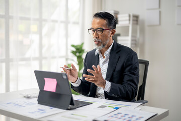 Obraz premium A man in a suit is sitting at a desk with a laptop and a stack of papers