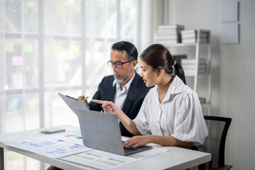 Fototapeta premium Two people are sitting at a desk with a laptop and papers