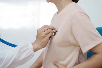 Asian female doctor listens to belly of pregnant mother during a prenatal exam in clinic. doctor...