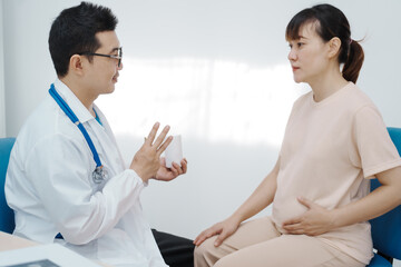 Fototapeta premium Asian female doctor listens to belly of pregnant mother during a prenatal exam in clinic. doctor provides caring advice, ensuring the health and happiness of the expecting mother and baby.