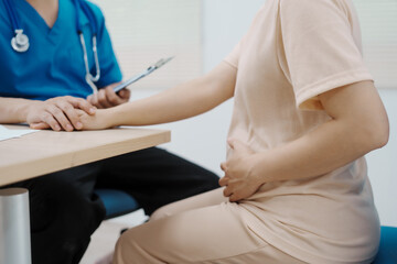 Asian female doctor listens to belly of pregnant mother during a prenatal exam in clinic. doctor...