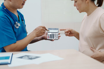 Asian female doctor listens to belly of pregnant mother during a prenatal exam in clinic. doctor...
