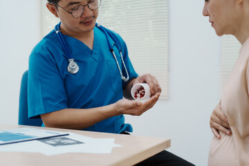 Fototapeta premium Asian female doctor listens to belly of pregnant mother during a prenatal exam in clinic. doctor provides caring advice, ensuring the health and happiness of the expecting mother and baby.