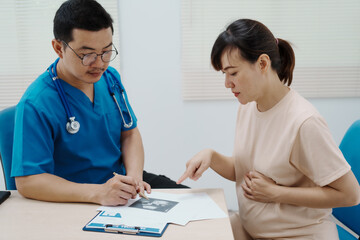 Asian female doctor listens to belly of pregnant mother during a prenatal exam in clinic. doctor...