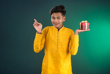 Young happy smiling handsome man holding gift box and posing on dark background