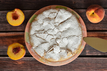 Fresh baked homemade charlotte pie with peaches. Cake sprinkled with powdered sugar served on rustic wooden table. Peach halves, juicy peach fruit, metal cake shovel. Top view.