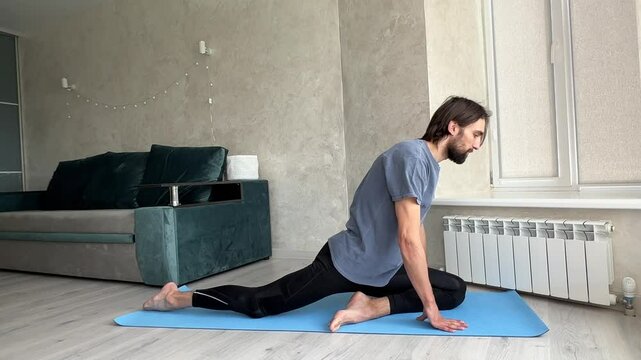 Yogi stretches hip flexors and quads in a variation of pigeon pose on a yoga mat, promoting flexibility and relaxation