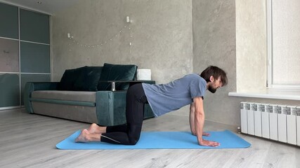 Man stretching his back in the cat cow pose during a yoga routine at home, promoting flexibility and relaxation