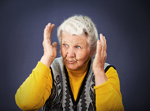 Closeup portrait, senior mature woman looking sideways, hearing voices, surprised in disbelief, hands on head, isolated blue background