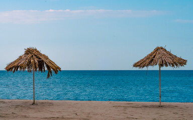 two straw beach umbrellas on an empty seashore on a clear day