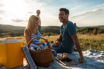 Obraz premium A married couple is enjoying a conversation and having a snack while their children are playing in the background, family picnic concept