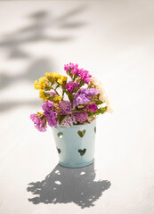 toy mini bucket with multi-colored flowers. on a light gray background in sunlight and shadow