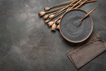Poppy seeds in bowl with wooden spoon, poppy heads, dark grunge background. Top view, flat lay,...