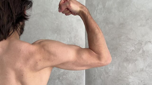 Man contracting biceps from various angles in front of a wall, showcasing muscle development and strength