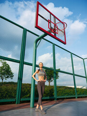 Fototapeta premium Young woman posing confidently at an outdoor basketball court with a hoop in the background under a blue sky