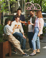 Warm sunny day and relaxing vibes with friends, Happy, smiling young people, men and women meeting at outdoor bar, restaurant and enjoying beer. Concept of relaxation, party, beer, party