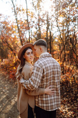 Fototapeta premium A young couple enjoying a romantic walk in the autumn forest, surrounded by fall foliage during sunset