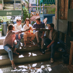 Sunny summer day vibes. Happy young people, men and women, friends gathering at local outdoor pub, bar to drinking refreshing beer. Relaxation and joy. Concept of relaxation, party, beer